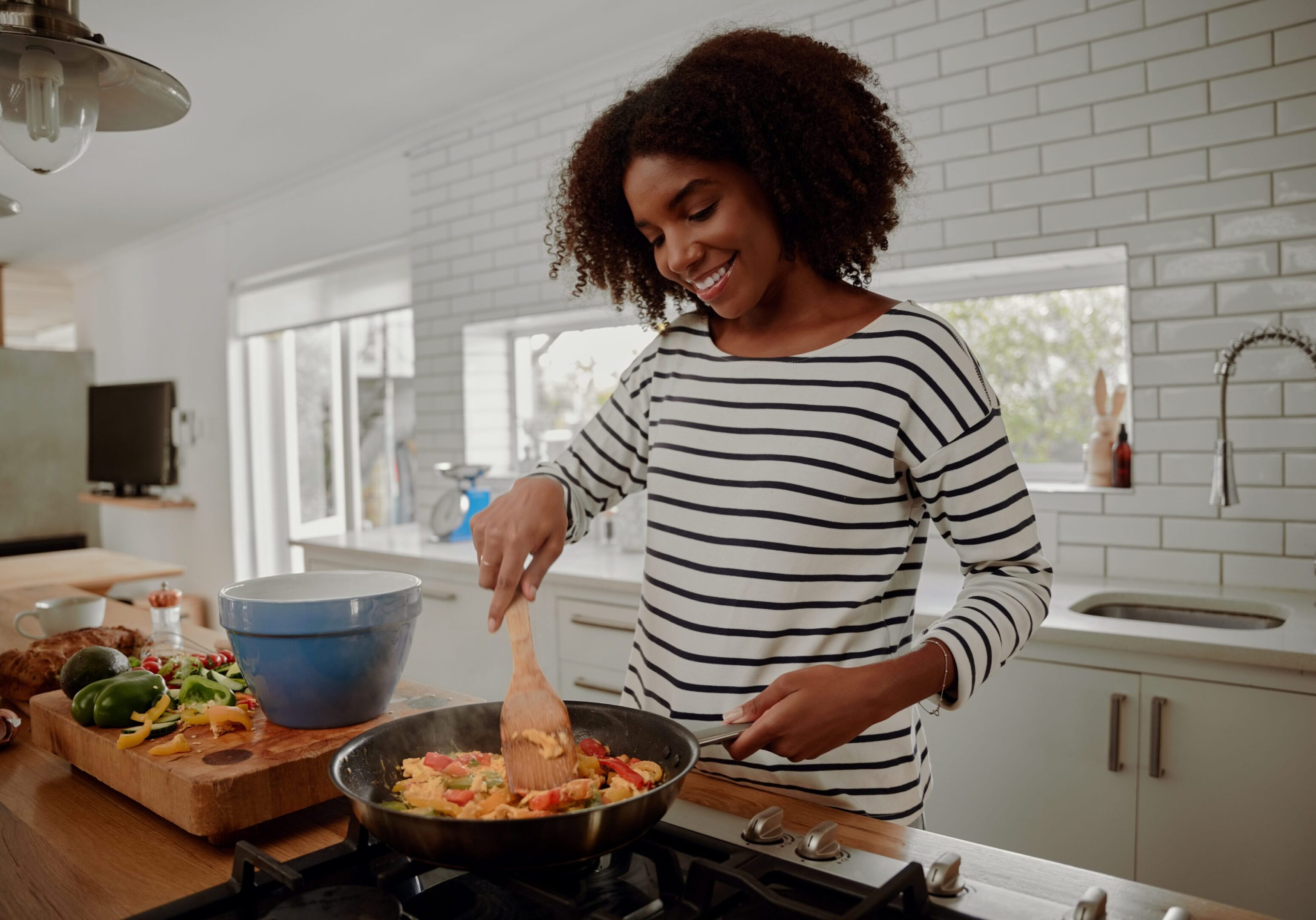 Woman mixing ingredients and vegetables in pan while preparing lunch indoors